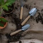 three gardening shovels surrounded by dirt and potted plants