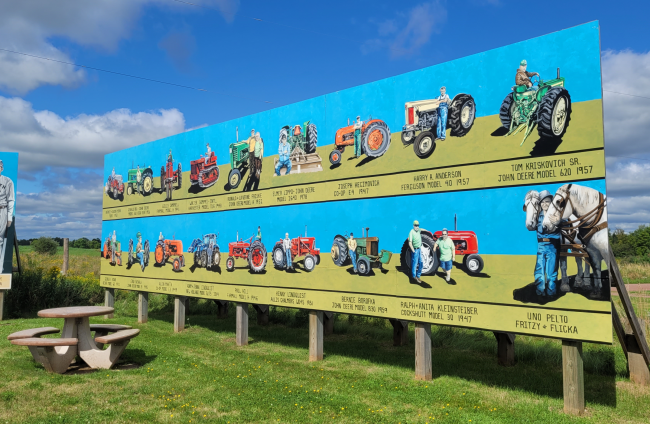 mural of farm equipment and farmers with a blue sky and green grass