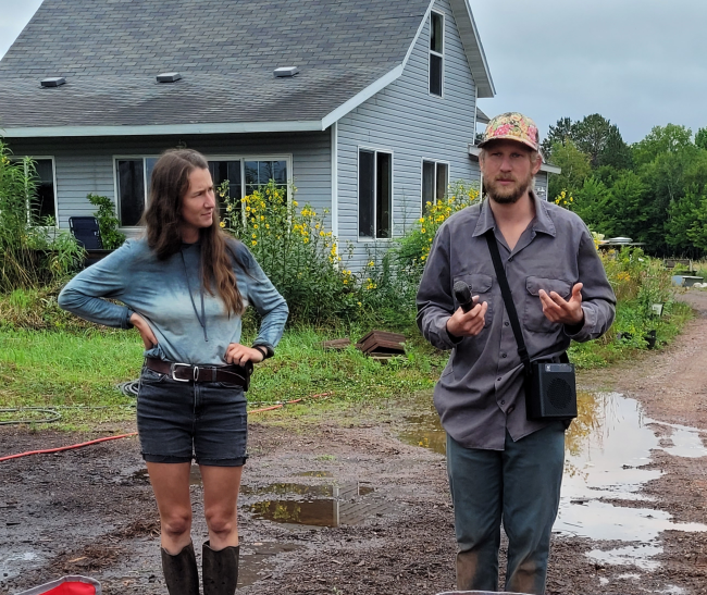 People standing in front of a light blue house. One is talking and the other is listening.