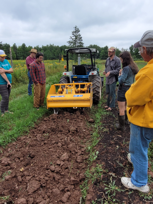 group stands around small yellow tractor while farmer talks