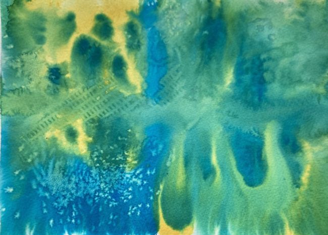 Blue and yellow watercolor flowing together on paper, some areas are green where the watercolor paints have mixed. Salt has been used on the lower left corner to create a spotted effect in the blue pigment.