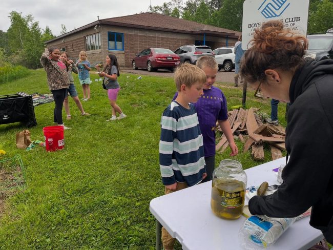 Youth standing at a table with a woman preparing food to try.