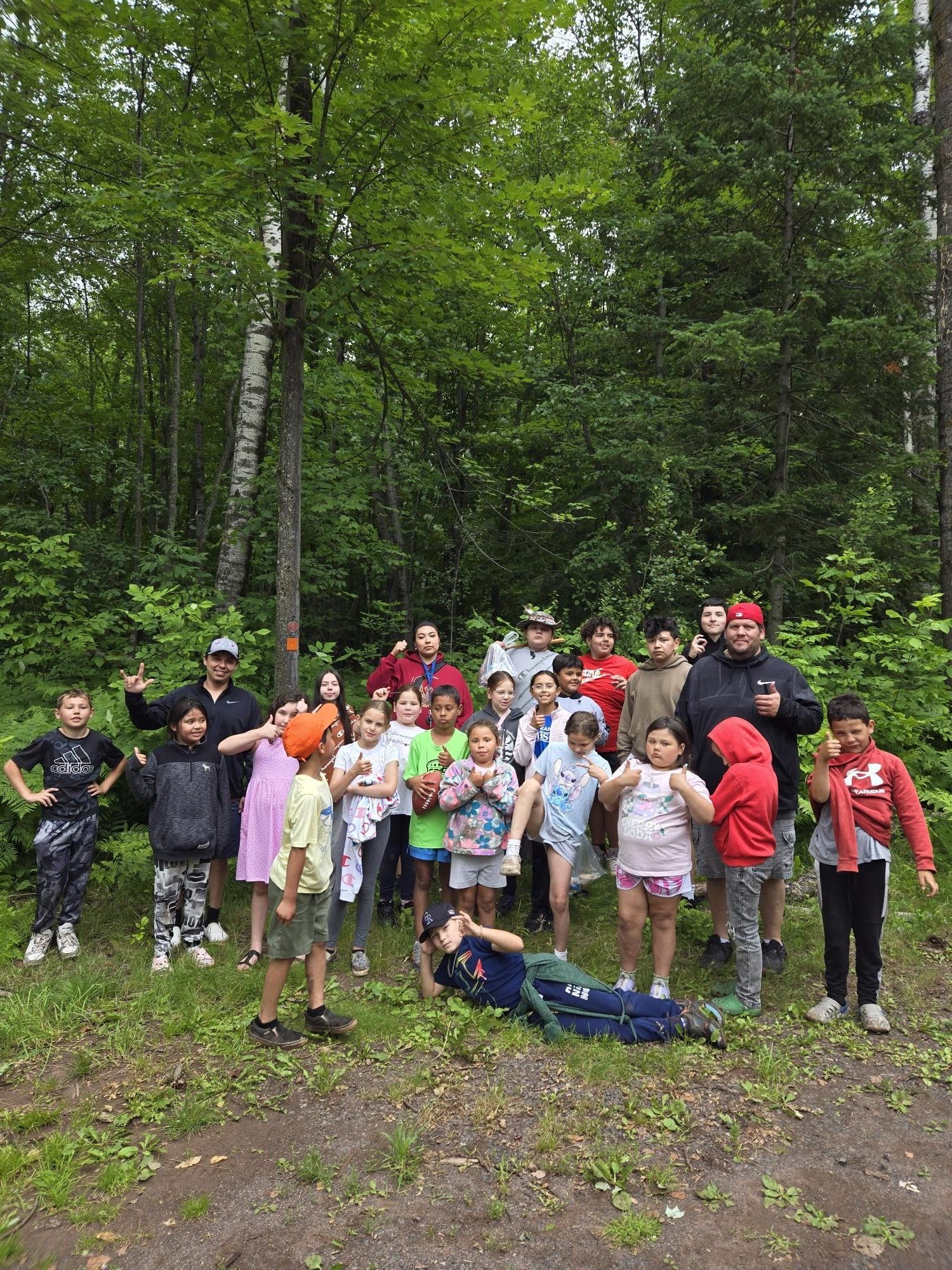 A large group of youth and adults standing at the beginning of a hiking trail smiling at the camera.