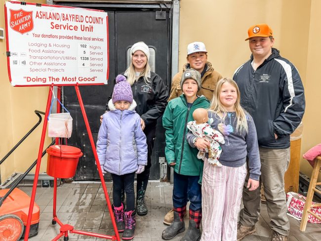 A group of youth and adults standing outside ringing a bell for charity.